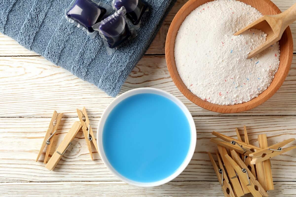 Na obrazku widoczne są spinacze do bielizny, ręcznik oraz miska z proszkiem do tkanin kolorowych.