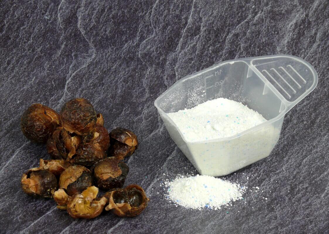 Proszek z formułą 2w1 obok orzechów piorących na szarej powierzchni.